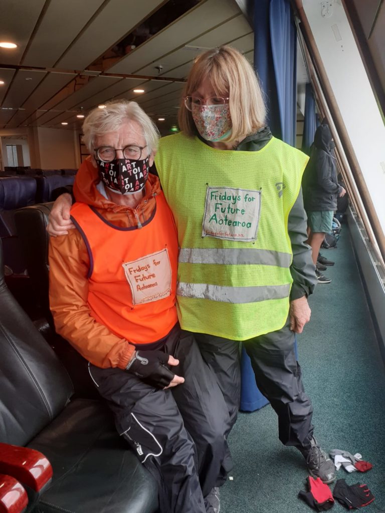 Photo of two members of Fridays for Future Aotearoa, wearing cycling gear and mini-Fridays for Future flags.