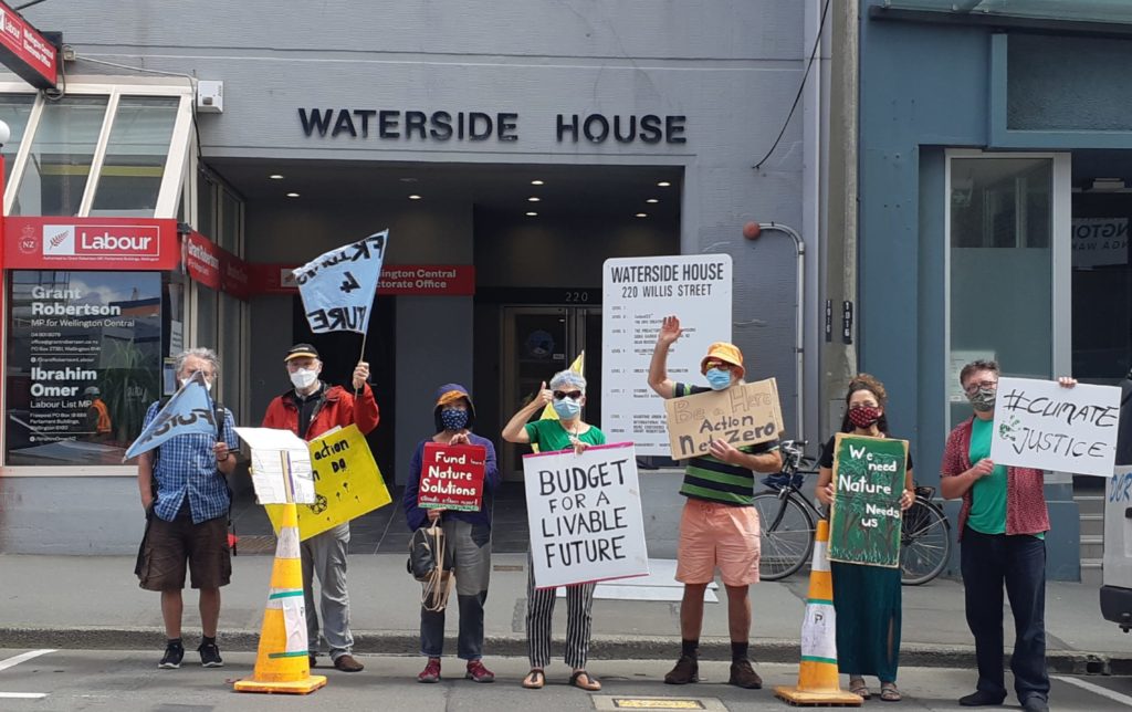 Seven Fridays for Future protesters standing in a car parking space in front of Grant Robertson's electorate office, holding flags and signs.